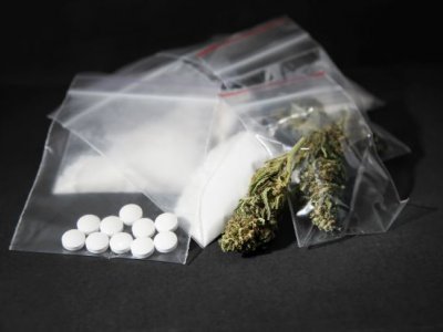 A photo of an array of leaf, powder and pill drugs in plastic bags on a black background.